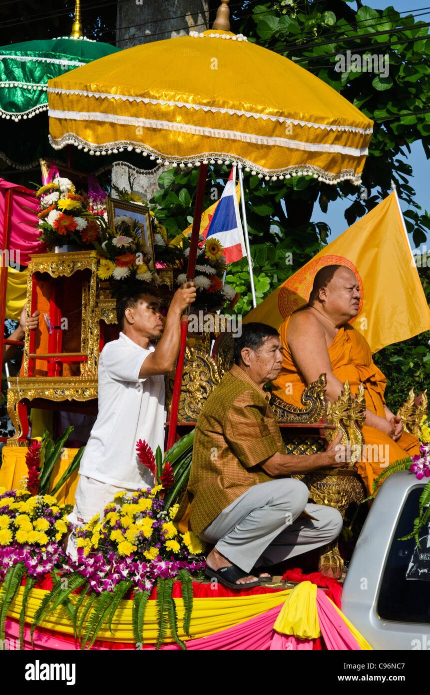 Grand moine assis avec l'homme tenant un grand parapluie décoré et un autre assistant sur char dans le nord de la Thaïlande Banque D'Images