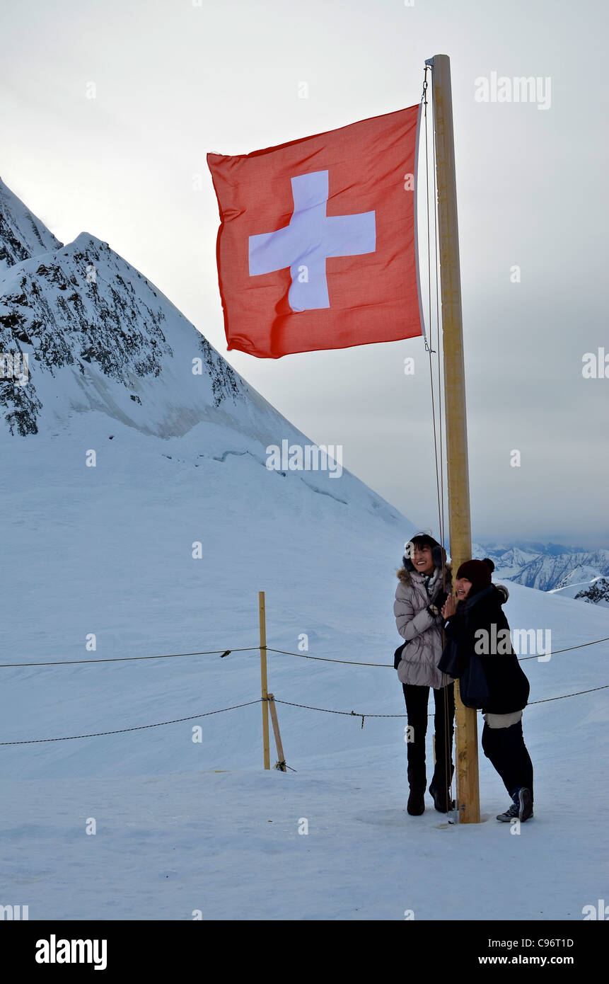 Les touristes asiatiques posent pour les photos à côté d'un drapeau qui flotte sur le plateau au Jungfraujoch. Banque D'Images