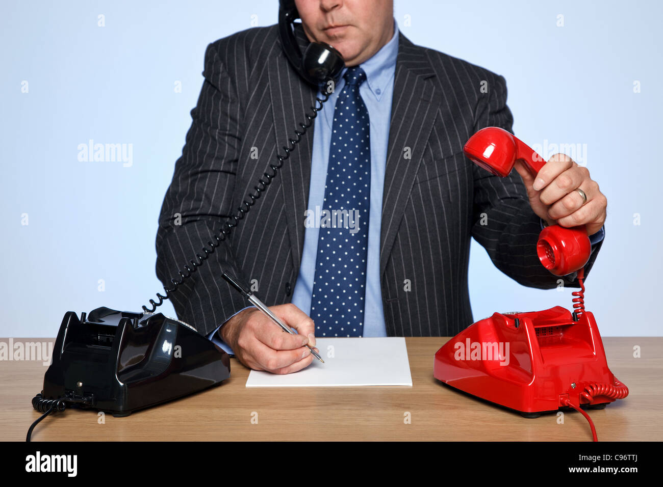 Photo d'un homme assis à un bureau avec deux téléphones traditionnels, un rouge et un noir. Banque D'Images