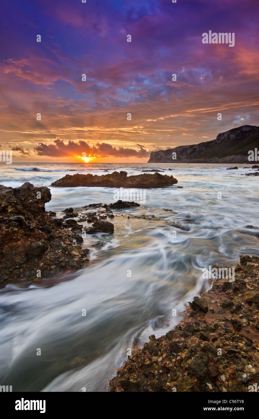 Seascape sunrise avec de l'eau en mouvement sur les rochers et du soleil à travers les nuages Banque D'Images