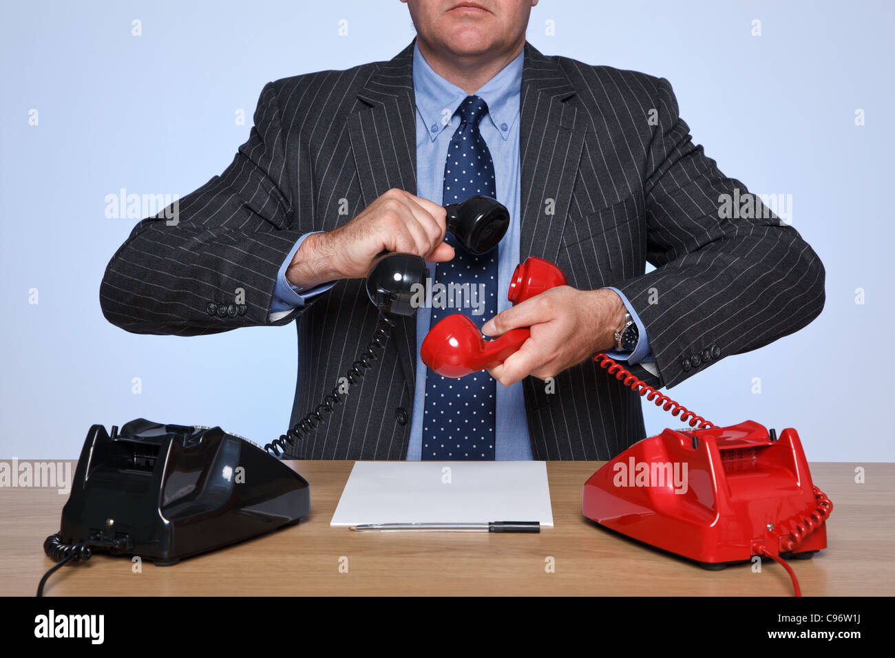 Photo d'un homme assis à un bureau avec deux téléphones traditionnels, un rouge et un noir. Concept de conférence téléphonique. Banque D'Images