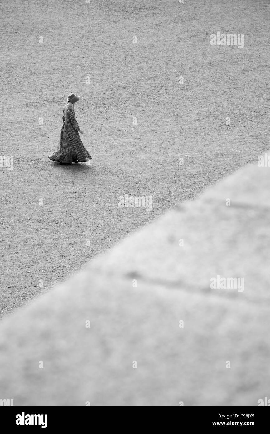 Photo en noir et blanc d'une femme marchant sur une enceinte de gravier dans l'habillement traditionnel anglais des années 1800. Banque D'Images