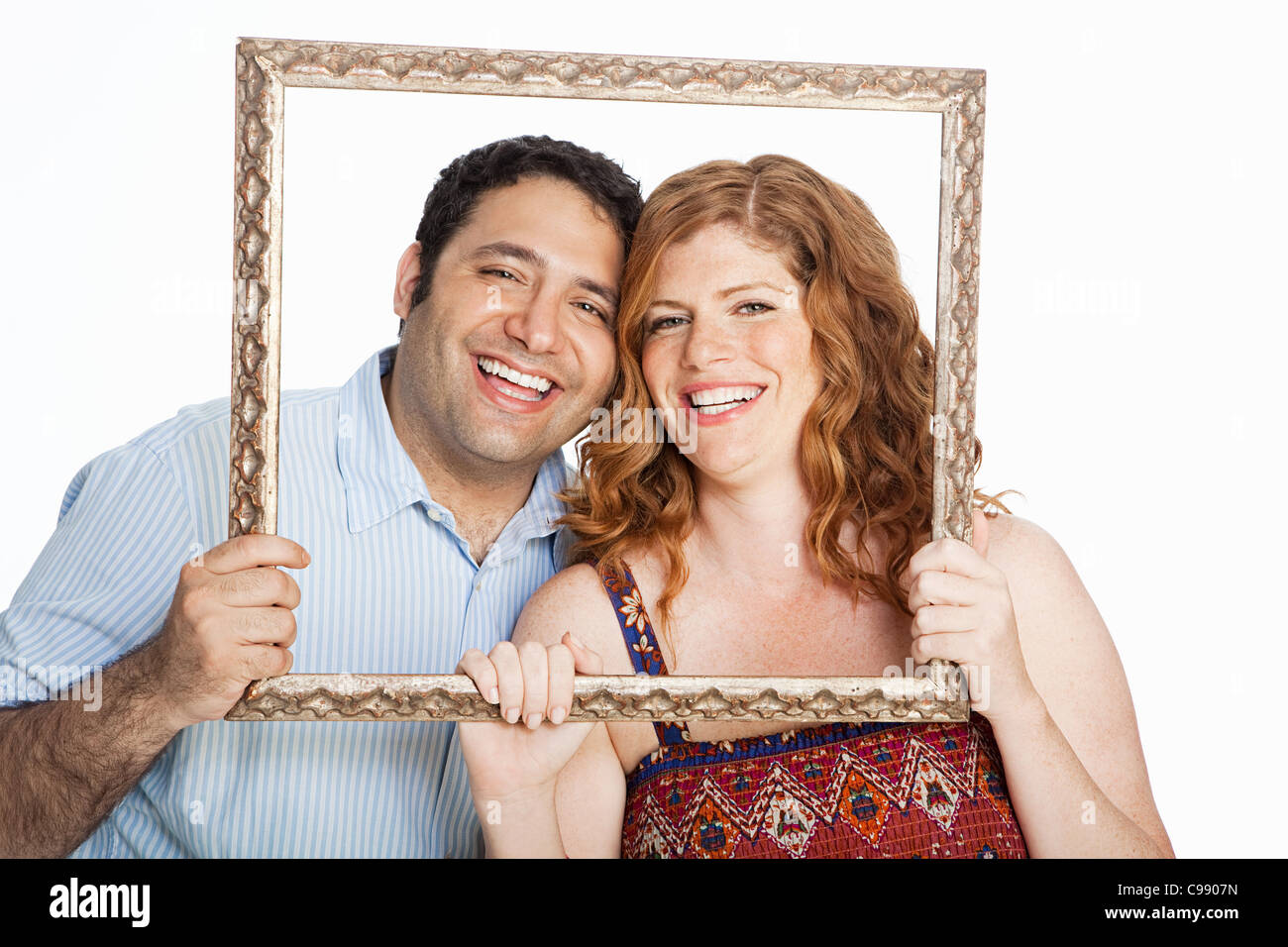 Couple smiling throrugh photo frame against white background Banque D'Images