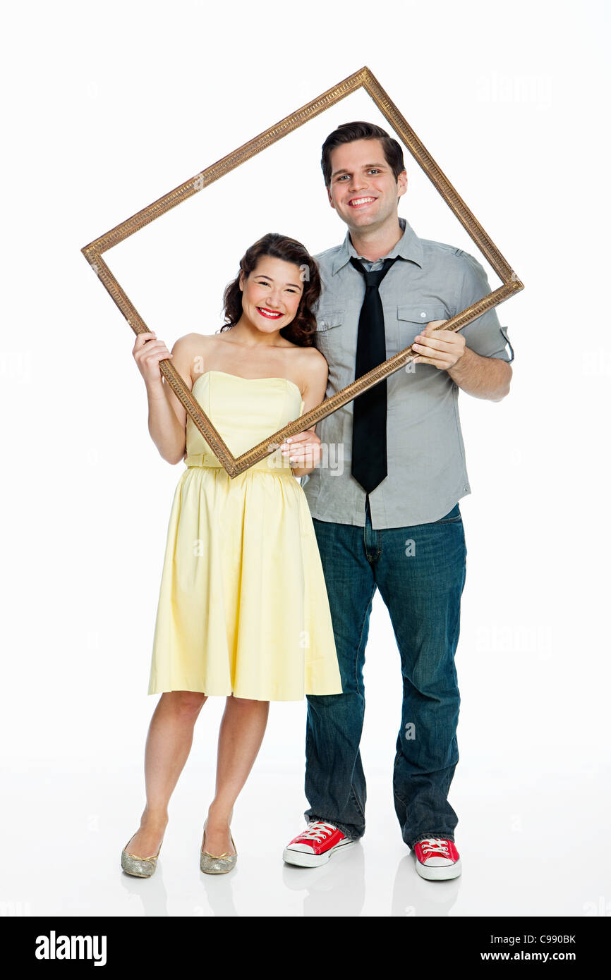 Young couple holding photo frame against white background Banque D'Images