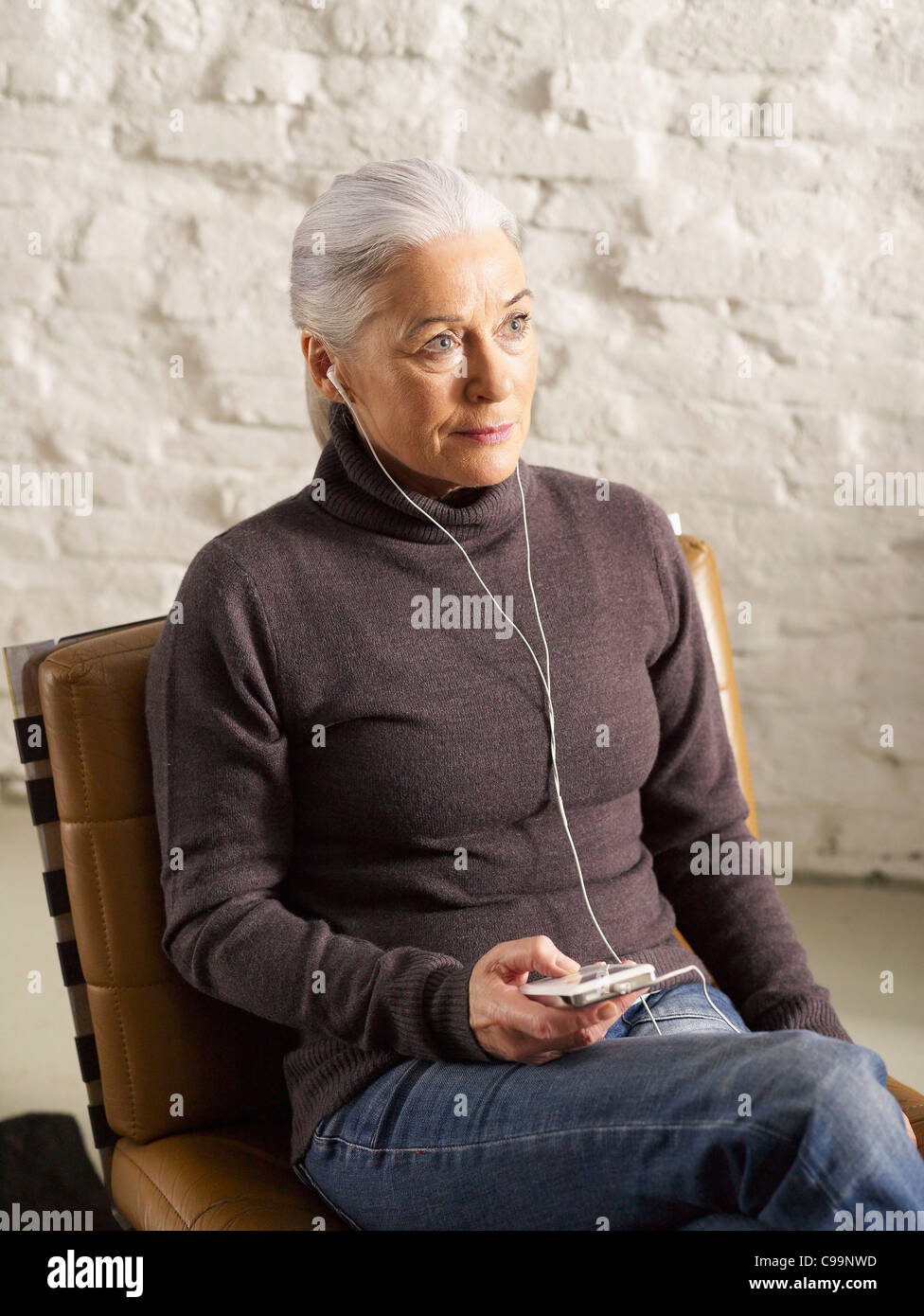 Allemagne, Hambourg, Senior woman sitting on chair et listening music Banque D'Images