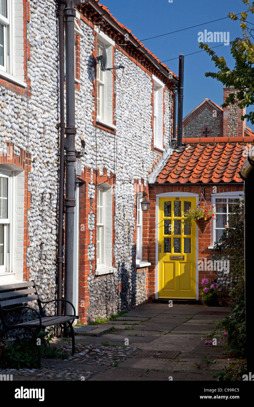 Avec pierre et brique cottage avec porte jaune vif, Blakeney, Norfolk Banque D'Images