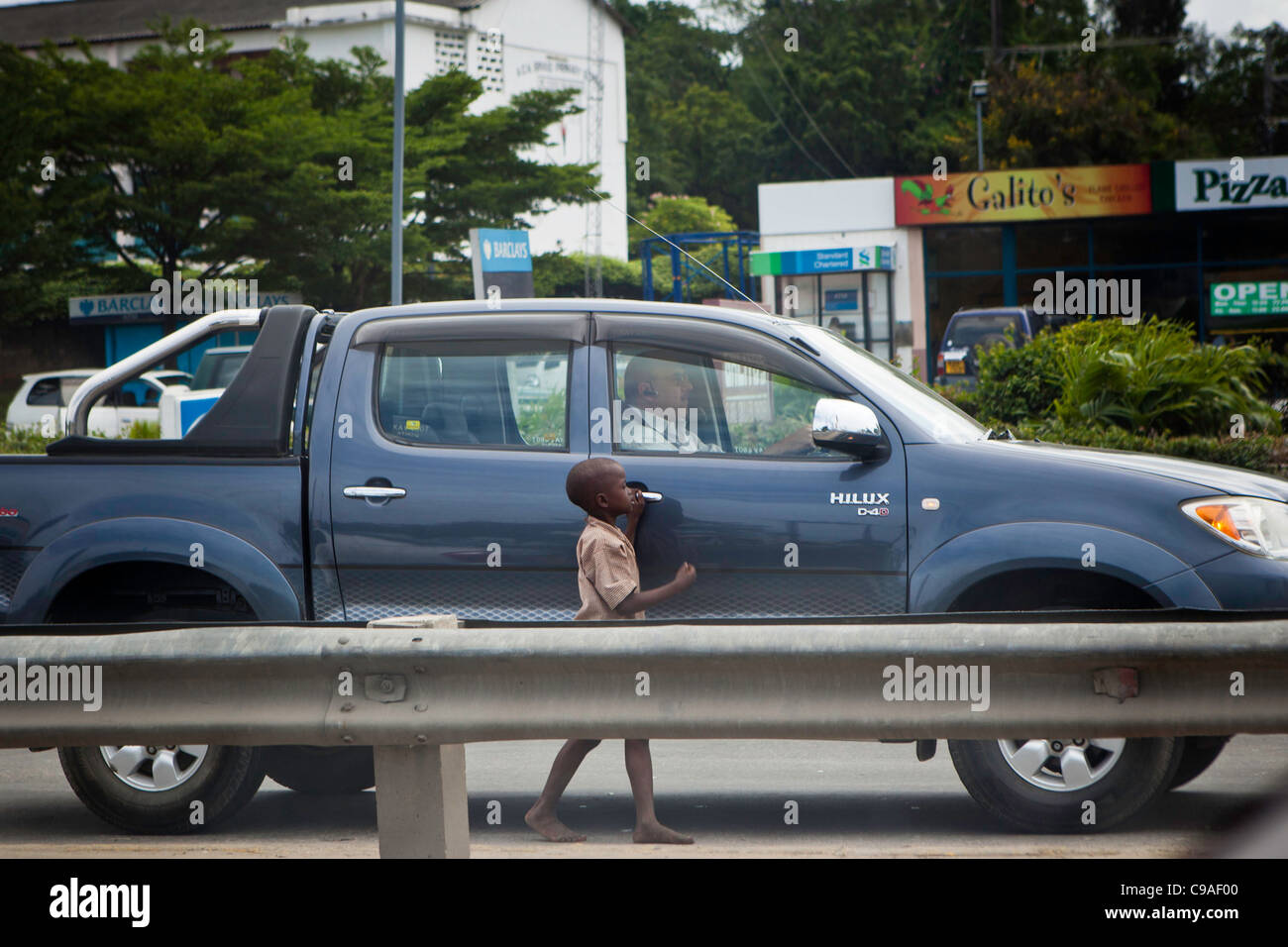 Un enfant des rues à Mombasa, Kenya mendier de l'argent d'un homme blanc qui passent. Banque D'Images