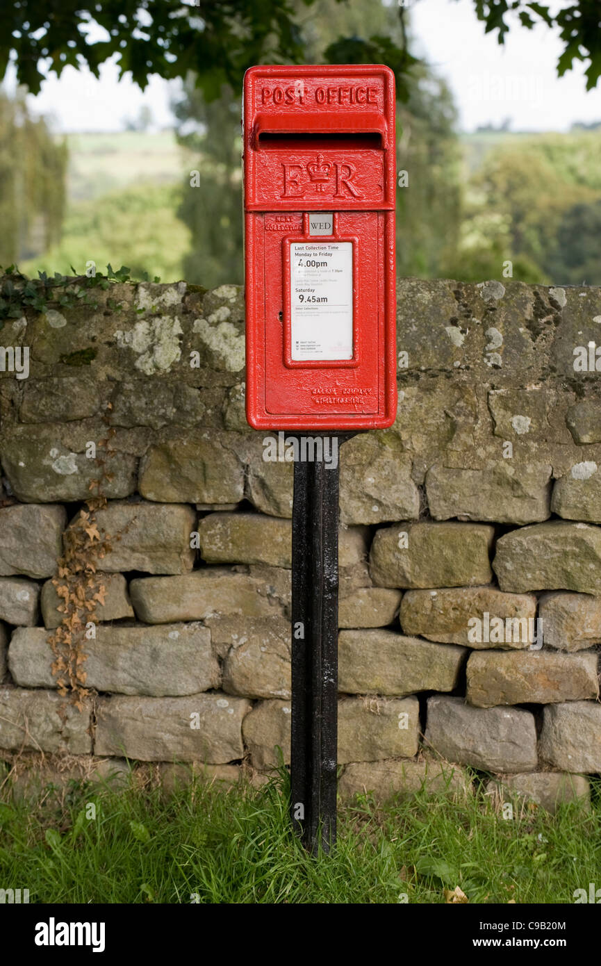 Close-up vue avant du rouge lumineux post box (Boîte de lampe style, marqué ER) debout devant un mur de pierres sèches - Leathley, North Yorkshire, Angleterre, Royaume-Uni. Banque D'Images