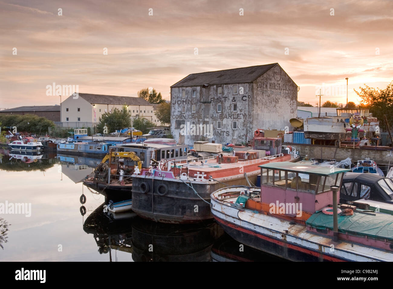 (Bateaux délabrés, besoin de réparation) amarré au chantier de la rivière Calder par ancien moulin industriel délabré, coucher de soleil - Wakefield, Yorkshire, Angleterre Banque D'Images