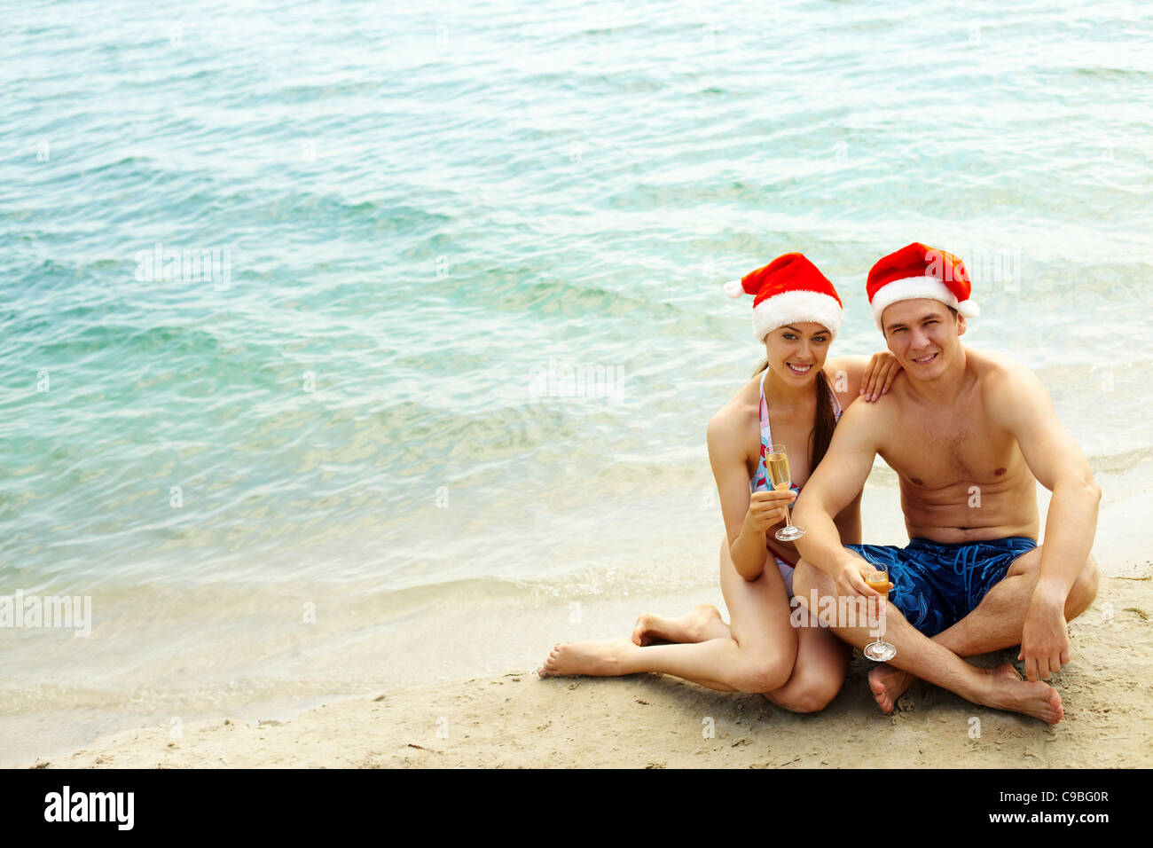 Portrait of attractive couple à Santa caps looking at camera sur la plage Banque D'Images
