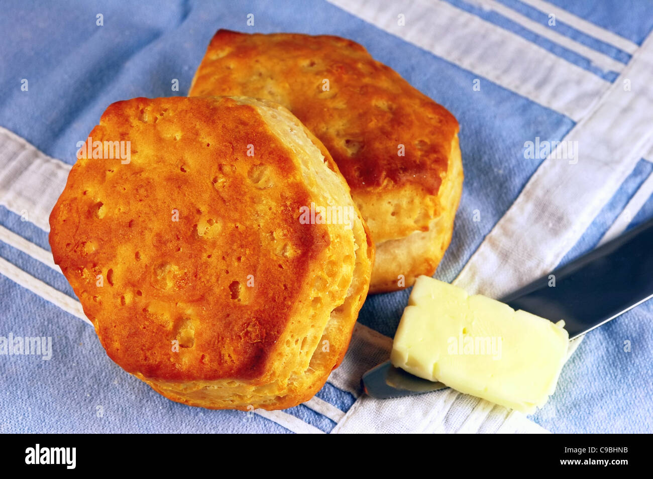 Deux biscuits au babeurre avec une noisette de beurre sur un couteau sur un linge de table bleu vintage Banque D'Images