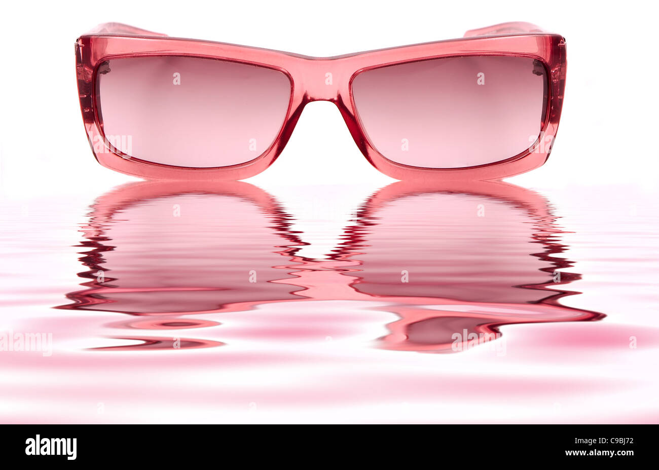 Une paire de lunettes rose chers isolé sur un fond blanc et reflétant dans l'eau ripples Banque D'Images