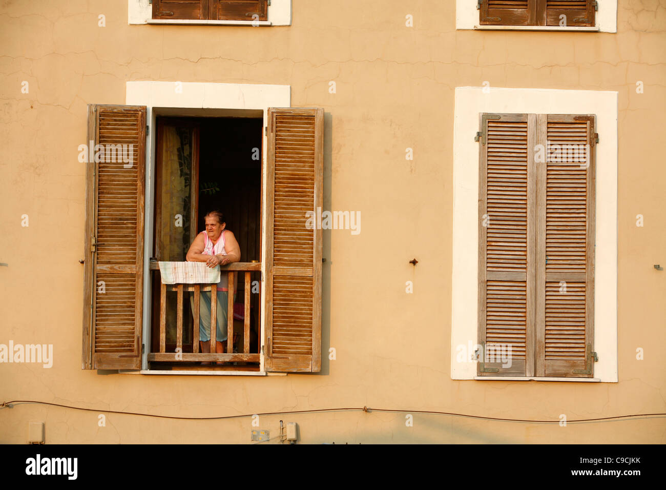 Femme debout dans sa fenêtre à une maison construite le long des murs de la ville. Alghero, Sardaigne, Italie. Banque D'Images