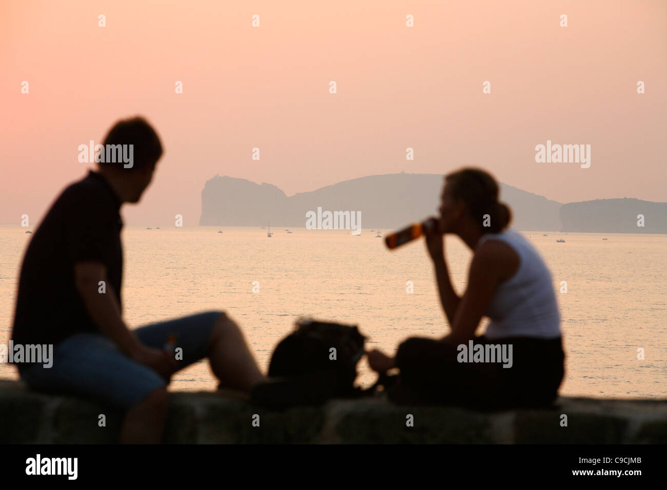 Couple assis sur les murs de la ville à la recherche sur le Capo Caccia, Alghero, Sardaigne, Italie. Banque D'Images