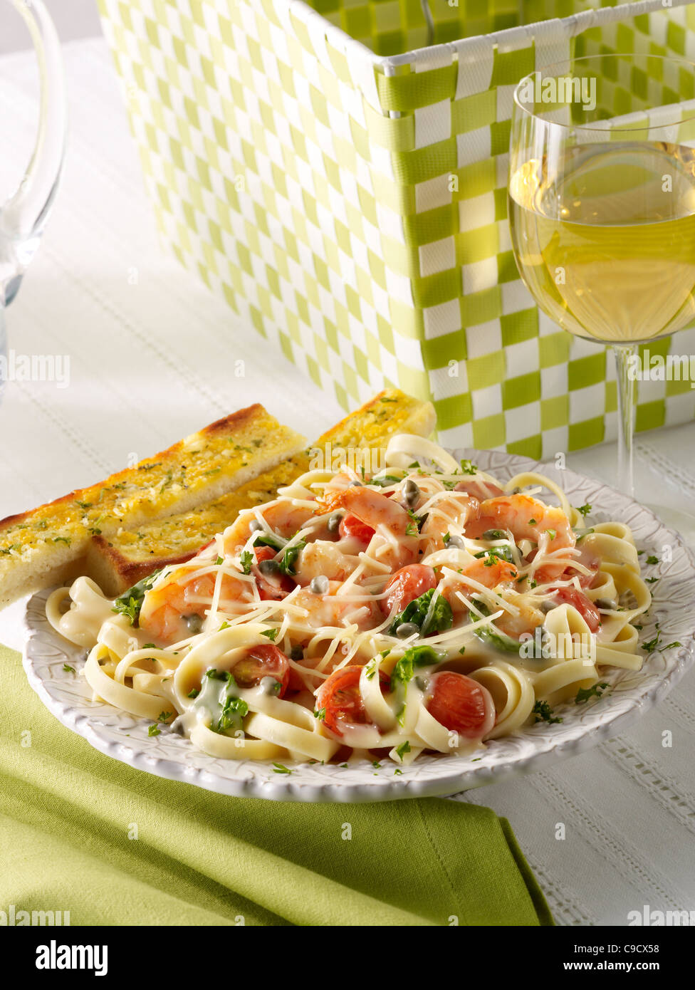 Pâtes aux crevettes avec légumes garni de fromage parmesan servi avec du pain à l'ail et un verre de vin blanc Banque D'Images