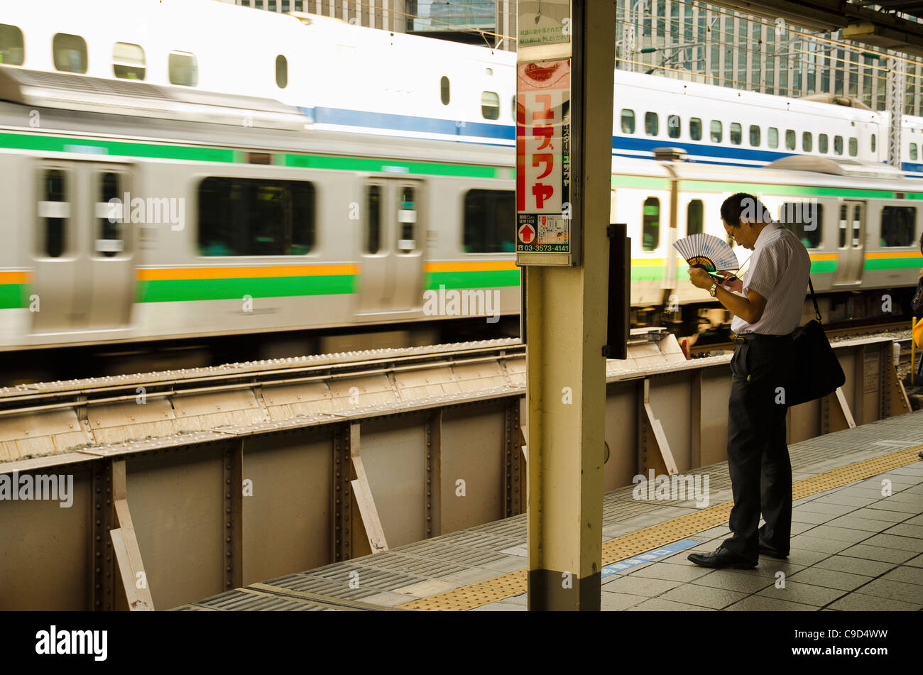 Le Japon, Honshu, Tokyo, Commuter sur la plate-forme lui-même de refroidissement avec ventilateur papier tout en attendant son train. Banque D'Images