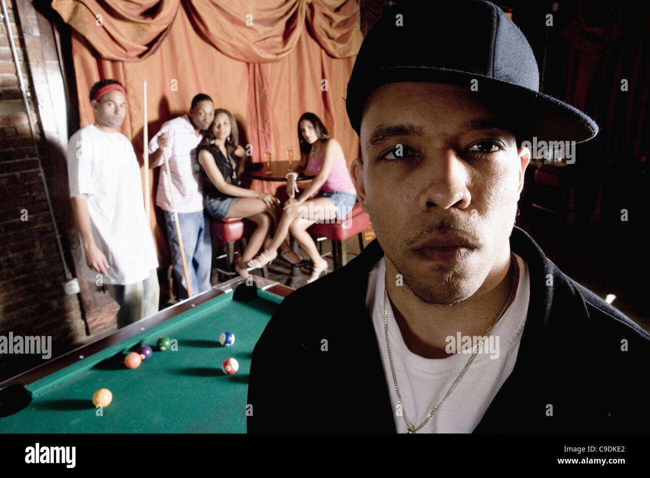 Close-up d'un jeune homme dans la mode hip-hop avec des gens jouer au billard en arrière-plan Banque D'Images