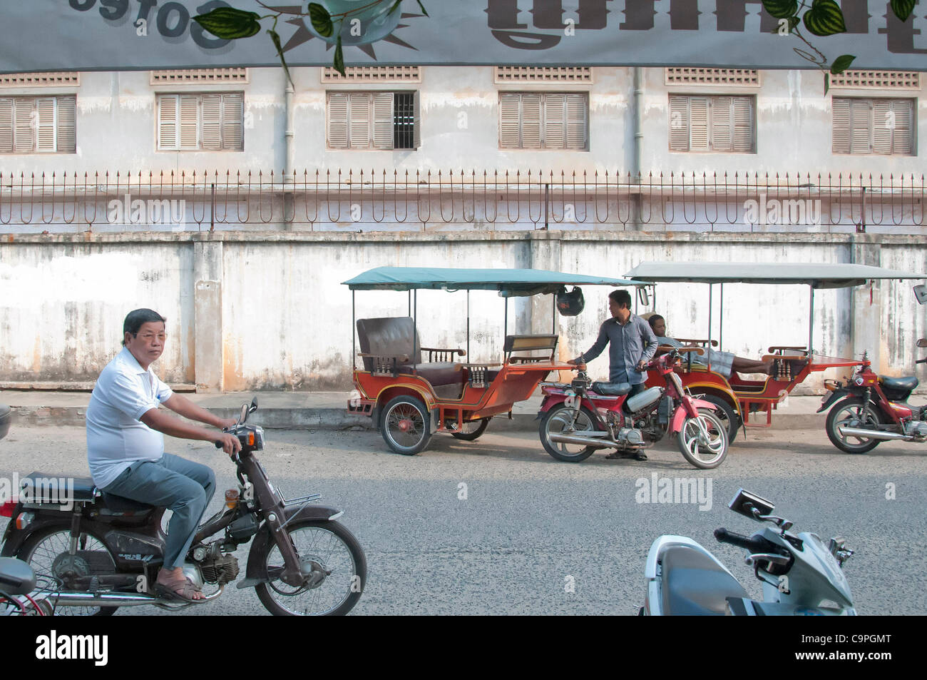 Un chauffeur de tuktuk se trouve à l'extérieur du site de l'ancienne école secondaire qui a été utilisée comme la célèbre prison de sécurité 21 (S-21) par les Khmers rouges. Le 4 février 2012, la Chambre d'appel des chambres extraordinaires des tribunaux cambodgiens a prononcé une peine à perpétuité Banque D'Images
