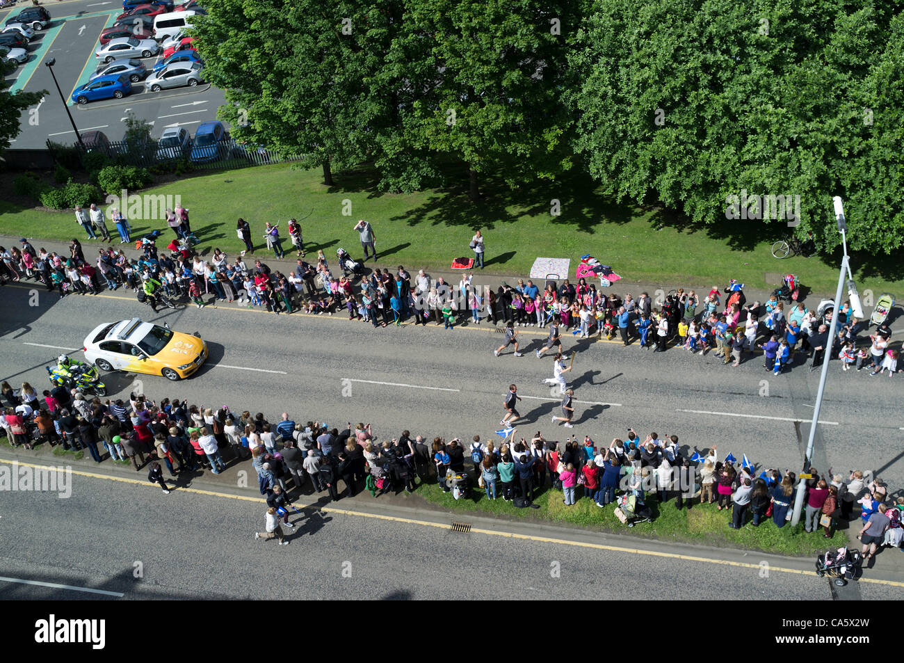 Dunfermline, Royaume-Uni. Des centaines de personnes bordent la route comme un coureur de la flamme olympique fait son chemin vers le bas, Dunfermiline Carnegie, Fife, en Écosse. 13 juin 2012 La torche voyageait dans Dunfermline sur son chemin de St Andrews à Édimbourg. Banque D'Images