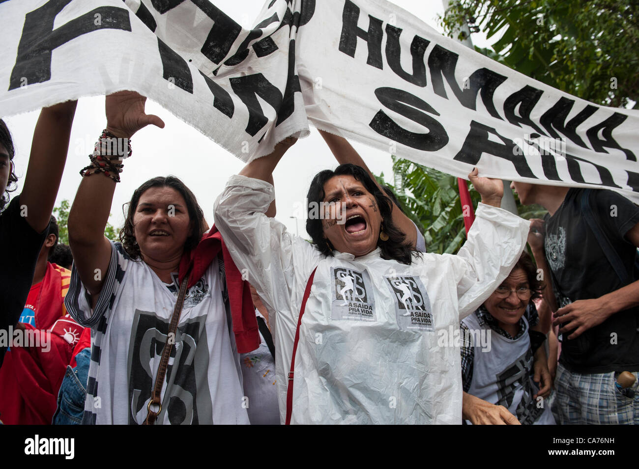 Rio de Janeiro, Brésil, le 20 juin 2012. Un manifestant anti-capitaliste avec une croix sur le symbole dollar peint sur sa joue tout en chants brandissant une bannière lors d'une démonstration par les populations autochtones, le mouvement du peuple sans terre (MST) et d'autres groupes de la société civile en face de la conférence des Nations Unies Riocentro. Les manifestants sont gardés hors de portée de voix et invisible à la conférence des Nations Unies. La Conférence des Nations Unies sur le développement durable (Rio +20), Rio de Janeiro, Brésil, le 20 juin 2012. Photo © Sue Cunningham. Banque D'Images