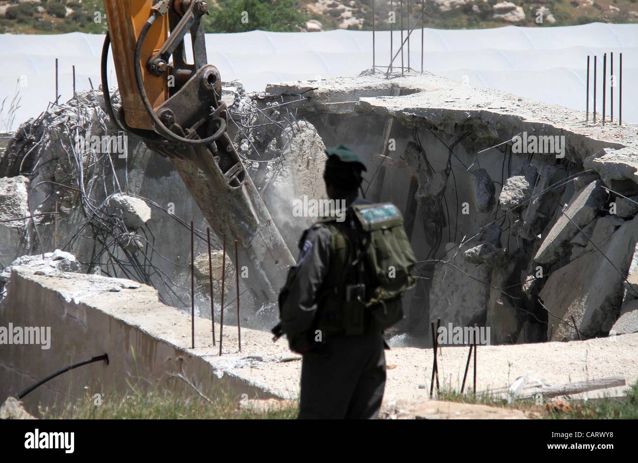 16 avril 2012 - Hébron, en Cisjordanie, territoire palestinien - Police des Frontières israélienne s'en tenir à la sécurité comme un bulldozer démolit un réservoir de stockage de l'eau appartenant à des Palestiniens dans le village de Dura, à l'extérieur de la ville de Cisjordanie d'Hébron, le 16 avril 2012. La construction du réservoir a été démoli pour être bu Banque D'Images