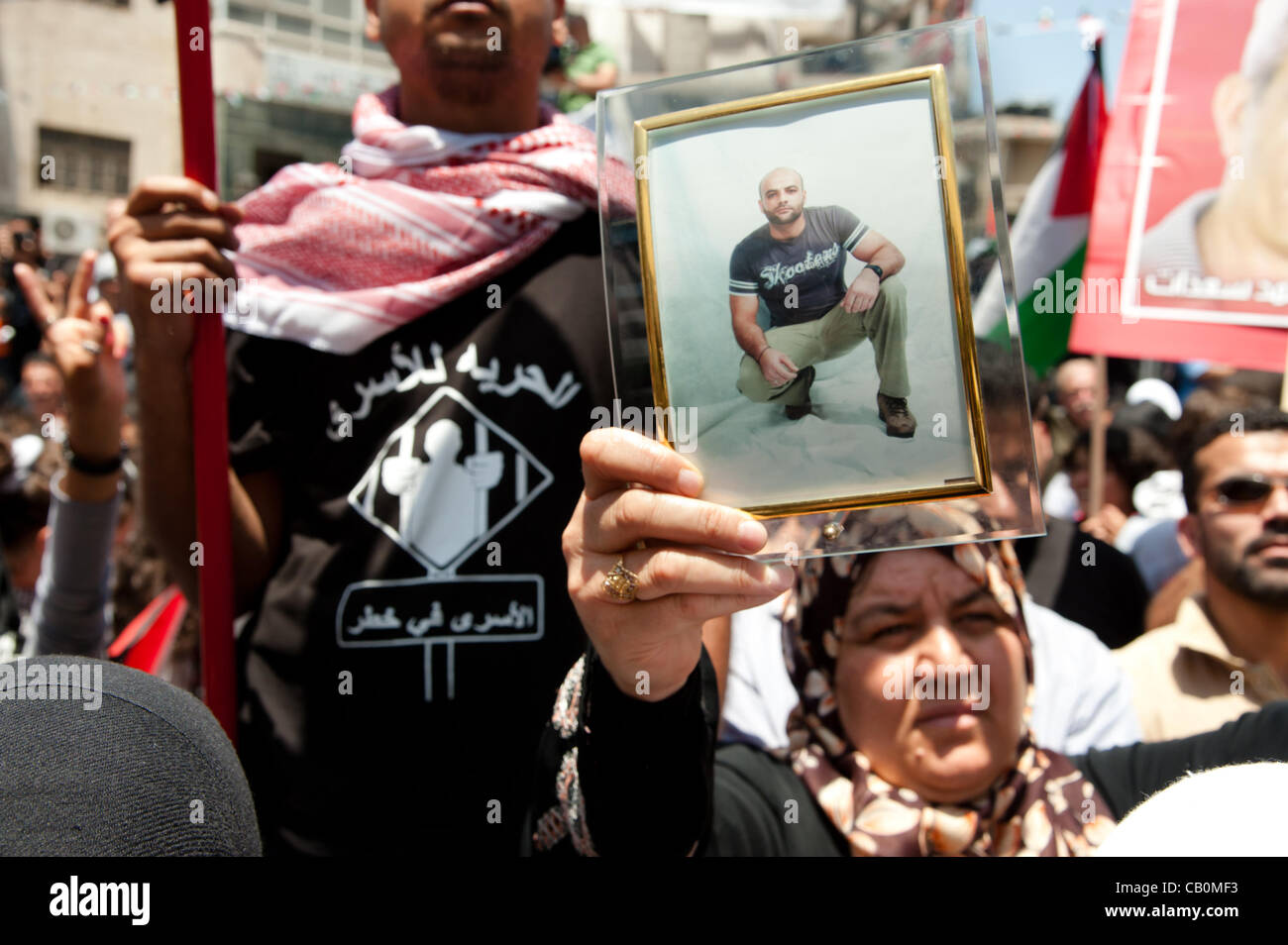 RAMALLAH, dans les territoires palestiniens - 15 MAI 2012 : une femme palestinienne porte un portrait de son fils emprisonné à côté d'un homme portant un t-shirt exprimant son soutien pour les prisonniers palestiniens dans les prisons israéliennes. Banque D'Images