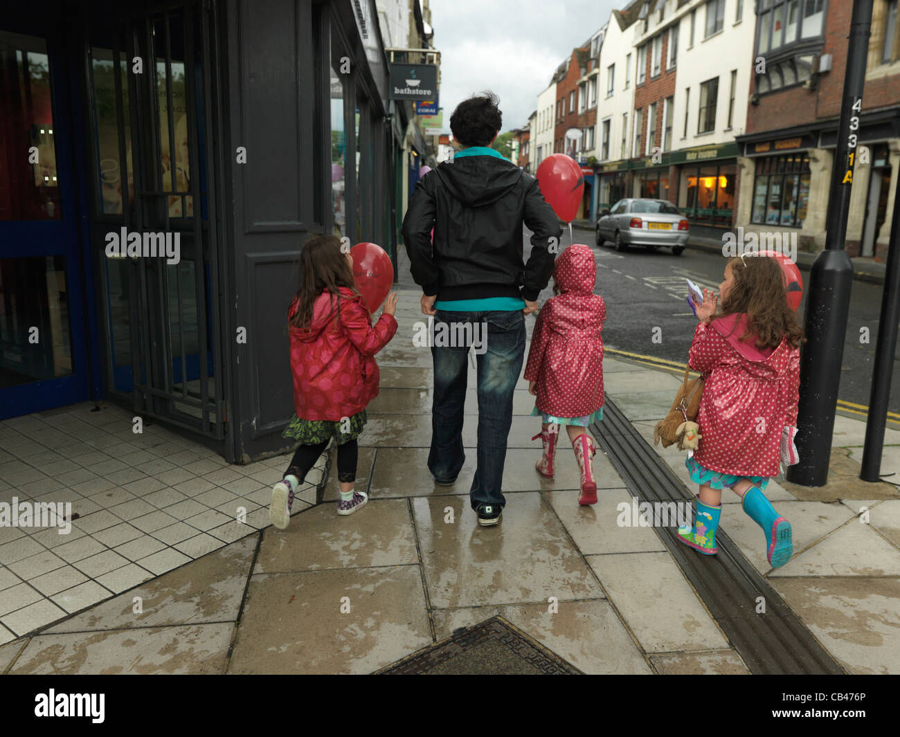 Enfants Holding Balloons Après Anniversaire Balade en Street dans la pluie en Angleterre Banque D'Images