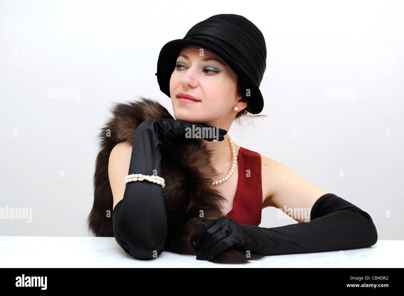 Jeune belle dame en noir gants et chapeau rétro et assis à côté avec un sourire malicieux Banque D'Images