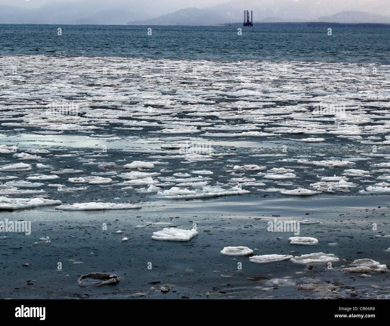 De grands morceaux de glace flottant dans l'eau bleue d'une baie d'Alaska avec une plate-forme de forage dans l'arrière-plan. Banque D'Images