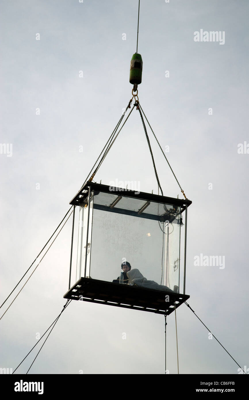 David Blaine assis dans sa boîte en plexiglas hissé dans le ciel au-dessus de champs Potters Park London UK Banque D'Images