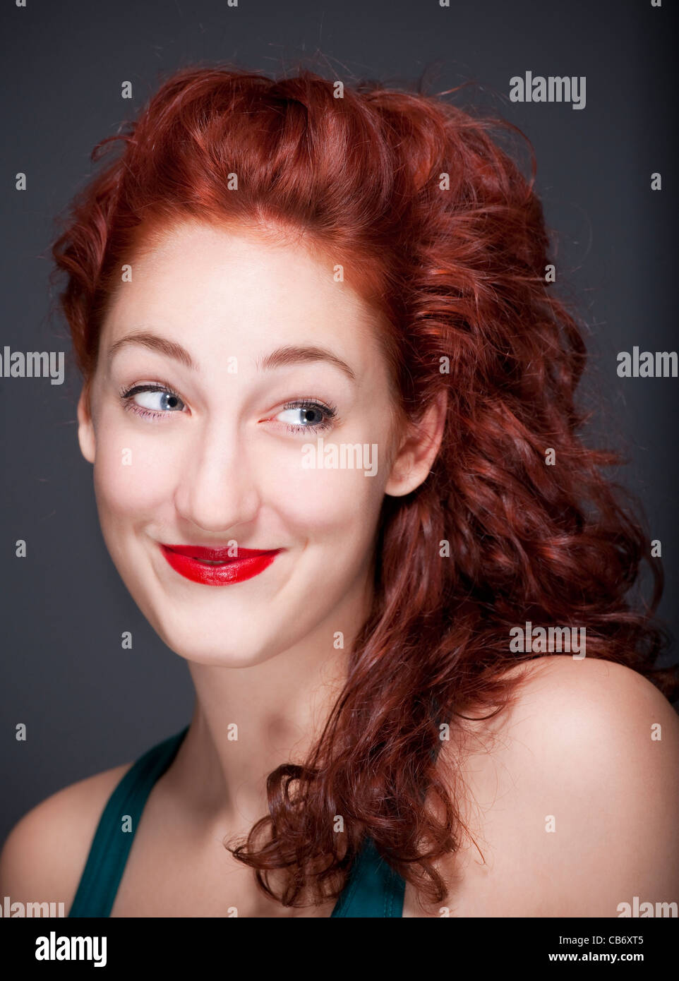 Teenage femme aux cheveux rouges, souriant à la recherche - isolé sur gris Banque D'Images