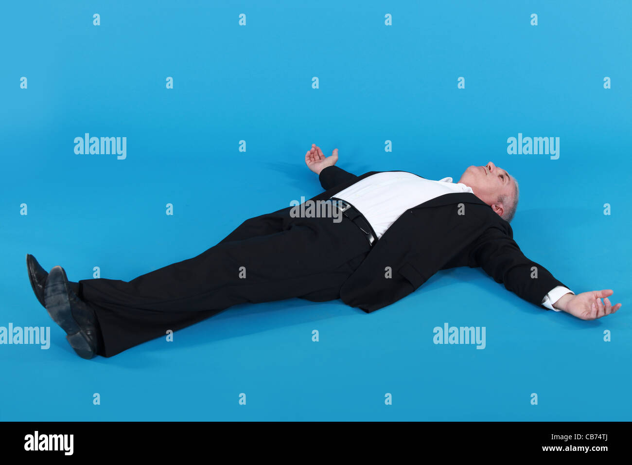 Man in suit allongé sur le dos, les bras bien écartés contre fond bleu Banque D'Images