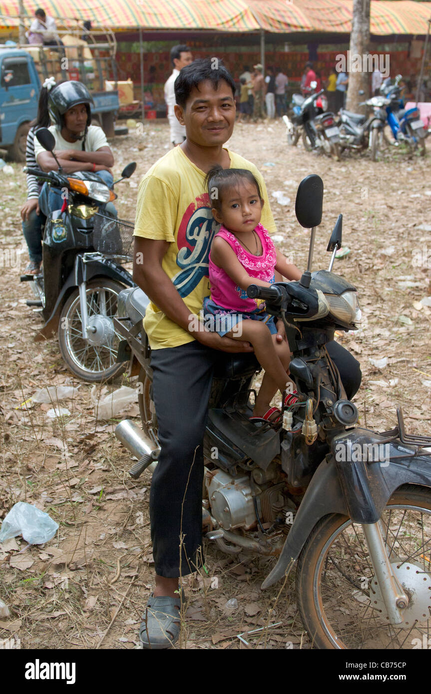 Smiling man avec sa fille assise sur un cyclomoteur à une fête de village, nouvel an cambodgien (Chaul Chnam Thmey), Bakong Village, Siem Reap, Cambodge Banque D'Images