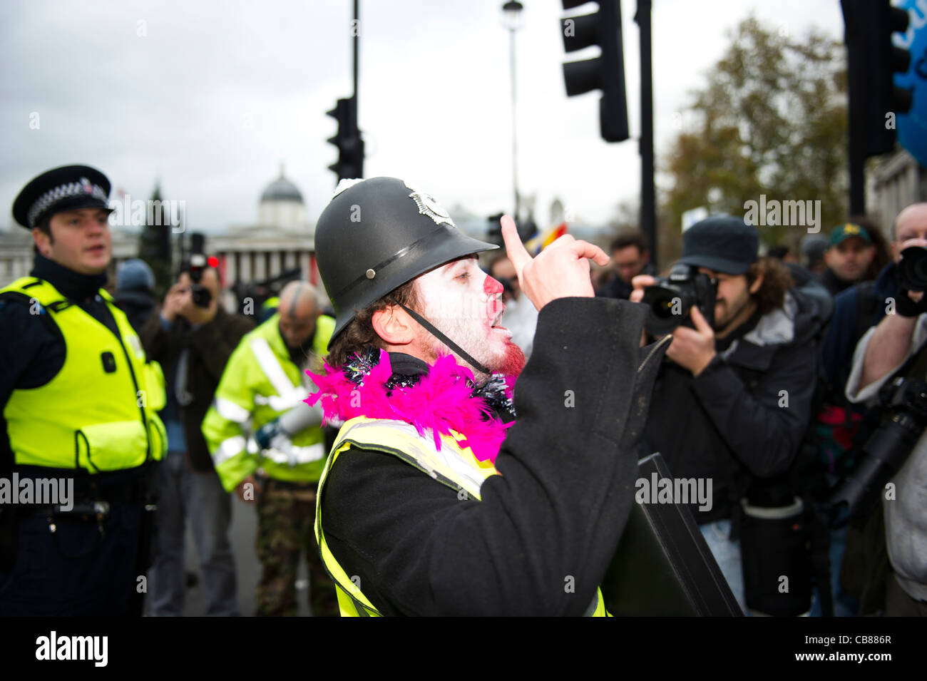 Un homme vêtu de démonstrateur de clown et plastique casque police à Trafalgar Square, Londres. Banque D'Images