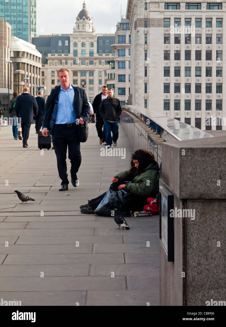 Les employés de bureau et de navetteurs traversant le pont de Londres dans la ville de London UK financial district avec femme sans-abri en premier plan Banque D'Images