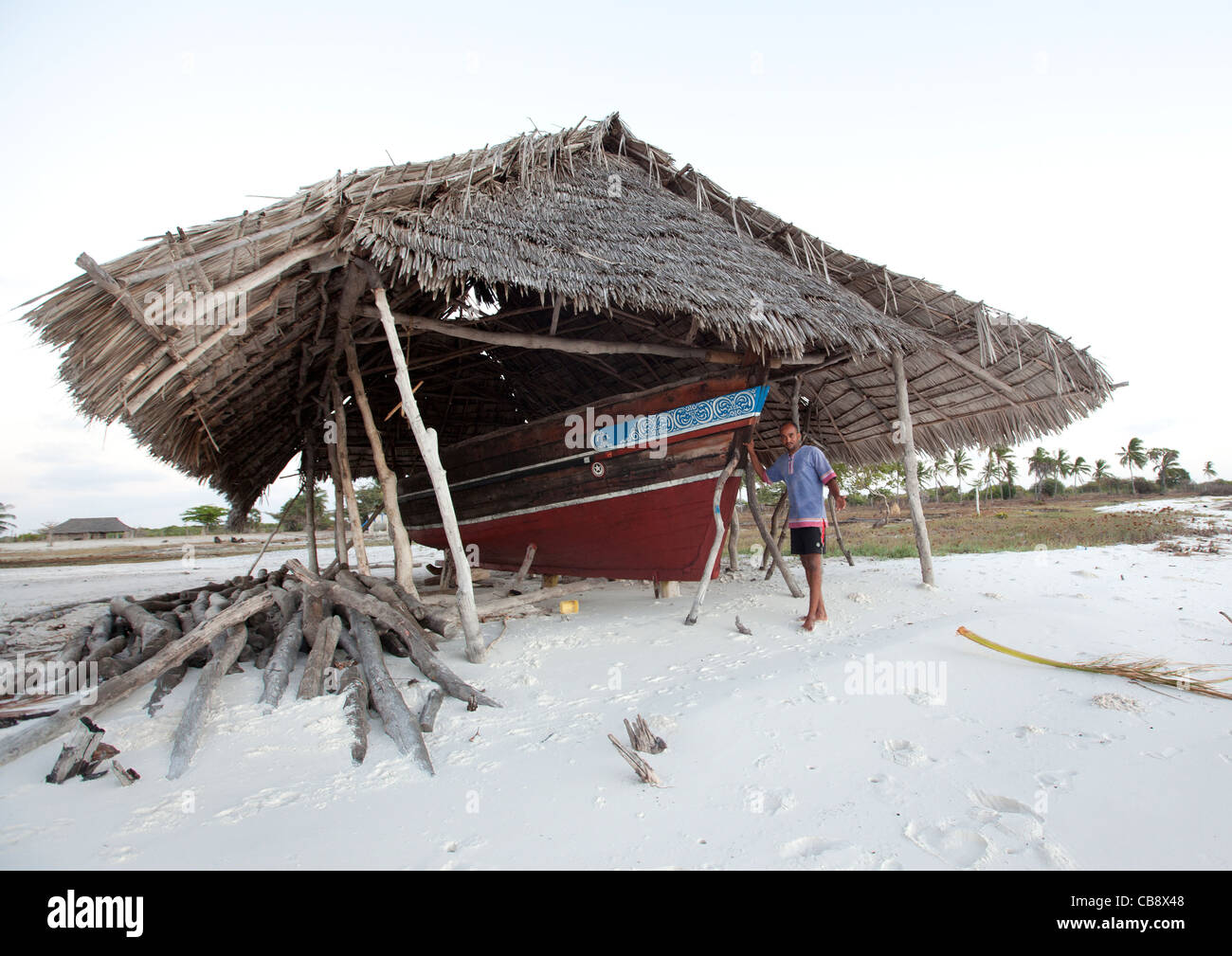 Chantier naval sur la plage avec un toit de palme, un homme debout, Lamu, Kenya Banque D'Images