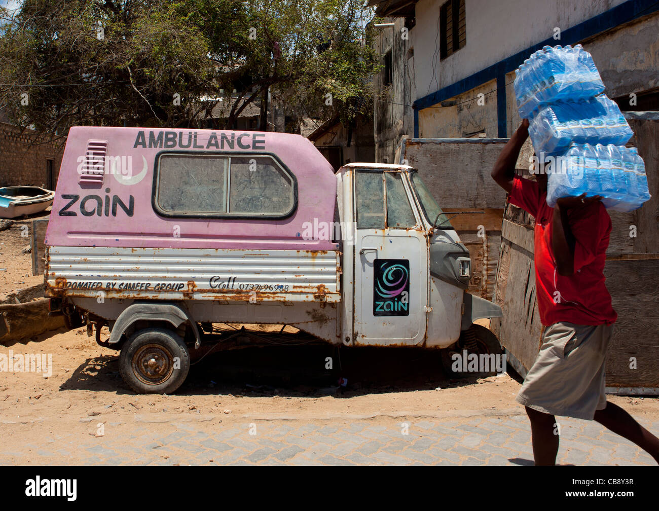 Un homme portant sur ses épaules l'eau potable en passant par une ambulance à Lamu, Kenya Banque D'Images
