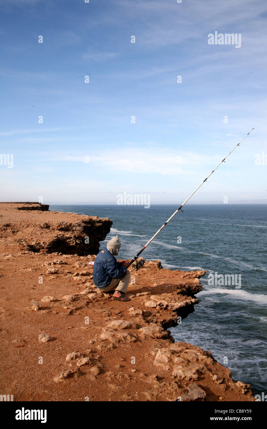 L'homme pêche sur le bord d'une falaise sur la côte atlantique du Maroc Banque D'Images