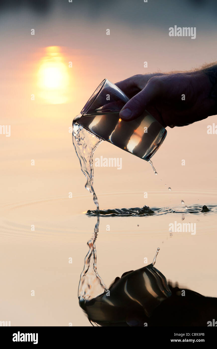 Verser un verre d'eau dans un lac encore au lever du soleil en Inde. Silhouette Banque D'Images
