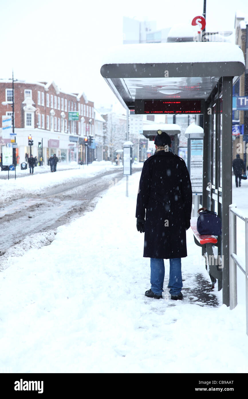 Vue arrière d'un homme en attente d'un bus par le côté de la route avec la neige qui tombe Banque D'Images
