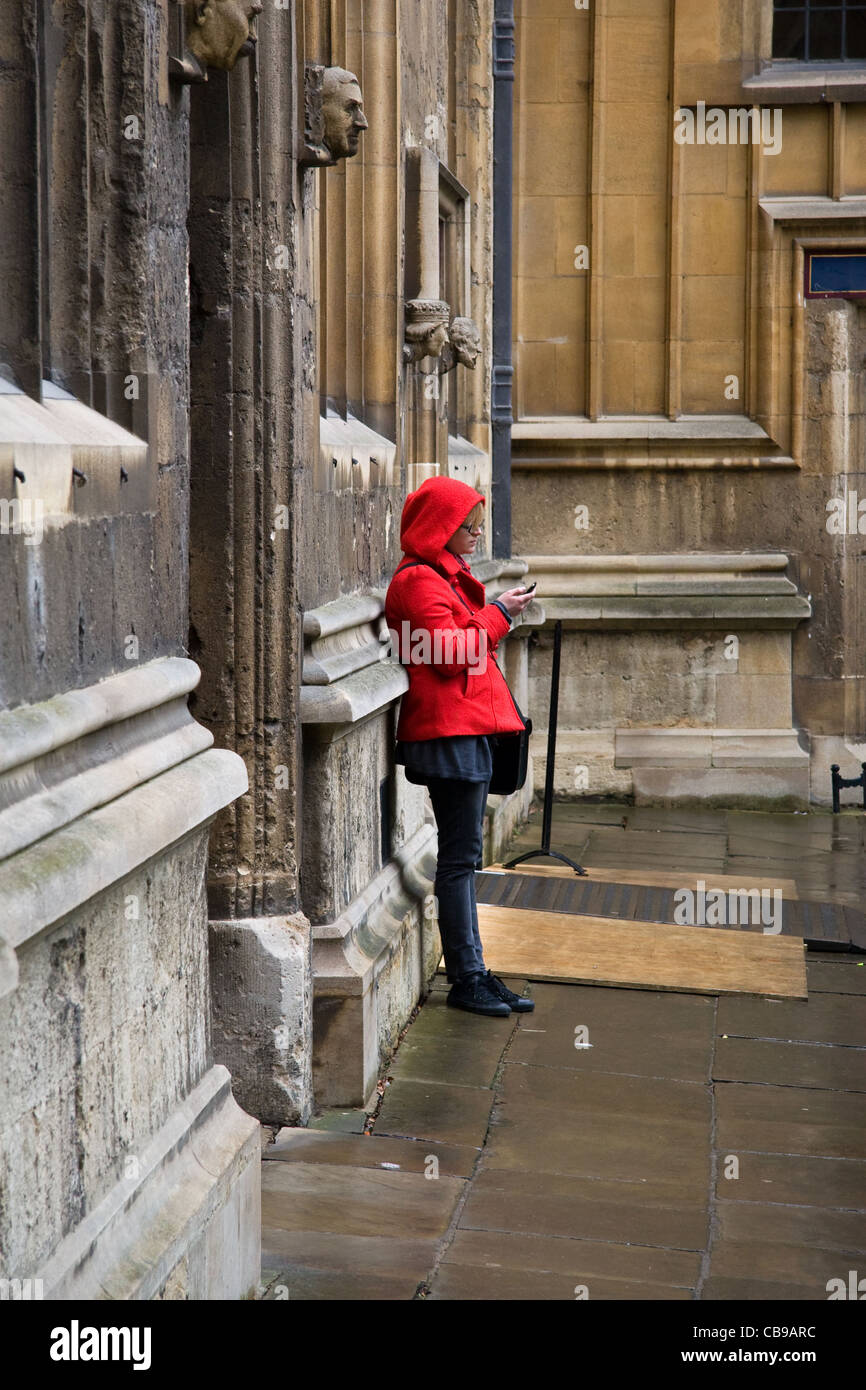 Jeune femme, des sms sur le téléphone, dans l'ancienne école quadrangle de la Bodleian Library, University of Oxford, Oxford, England, UK Banque D'Images