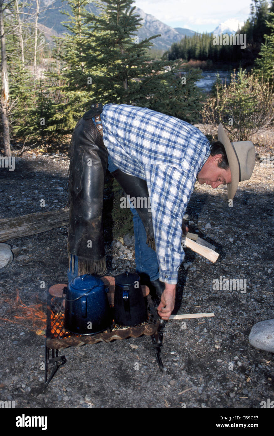 Un wrangler stokes un cuisinier à la chaleur du feu de l'émaillerie de pots 'Cowboy' café au cours d'une randonnée à cheval dans le parc national de Banff en Alberta, Canada. Banque D'Images