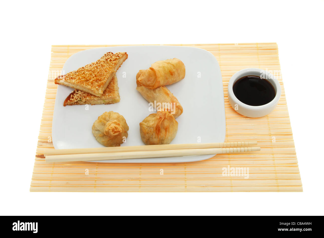 En-cas chinois, rouleau de printemps, et de crevettes wontons toast sur une assiette avec des baguettes et de la sauce soja dans un bol sur un mat en bambou Banque D'Images