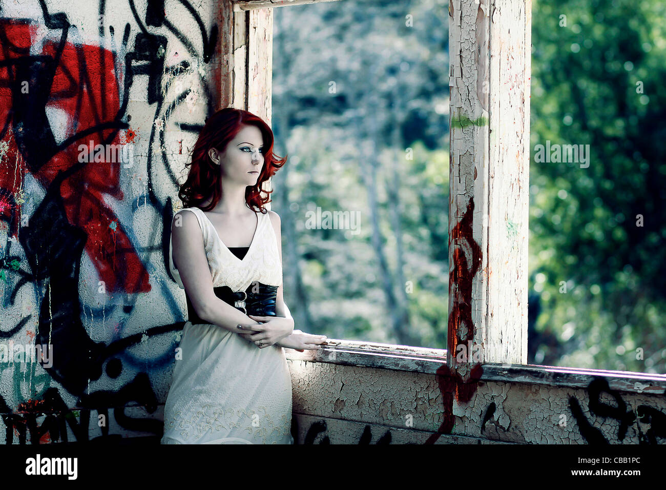 Une jeune fille debout à côté d'une fenêtre avec des graffitis sur les murs. Banque D'Images