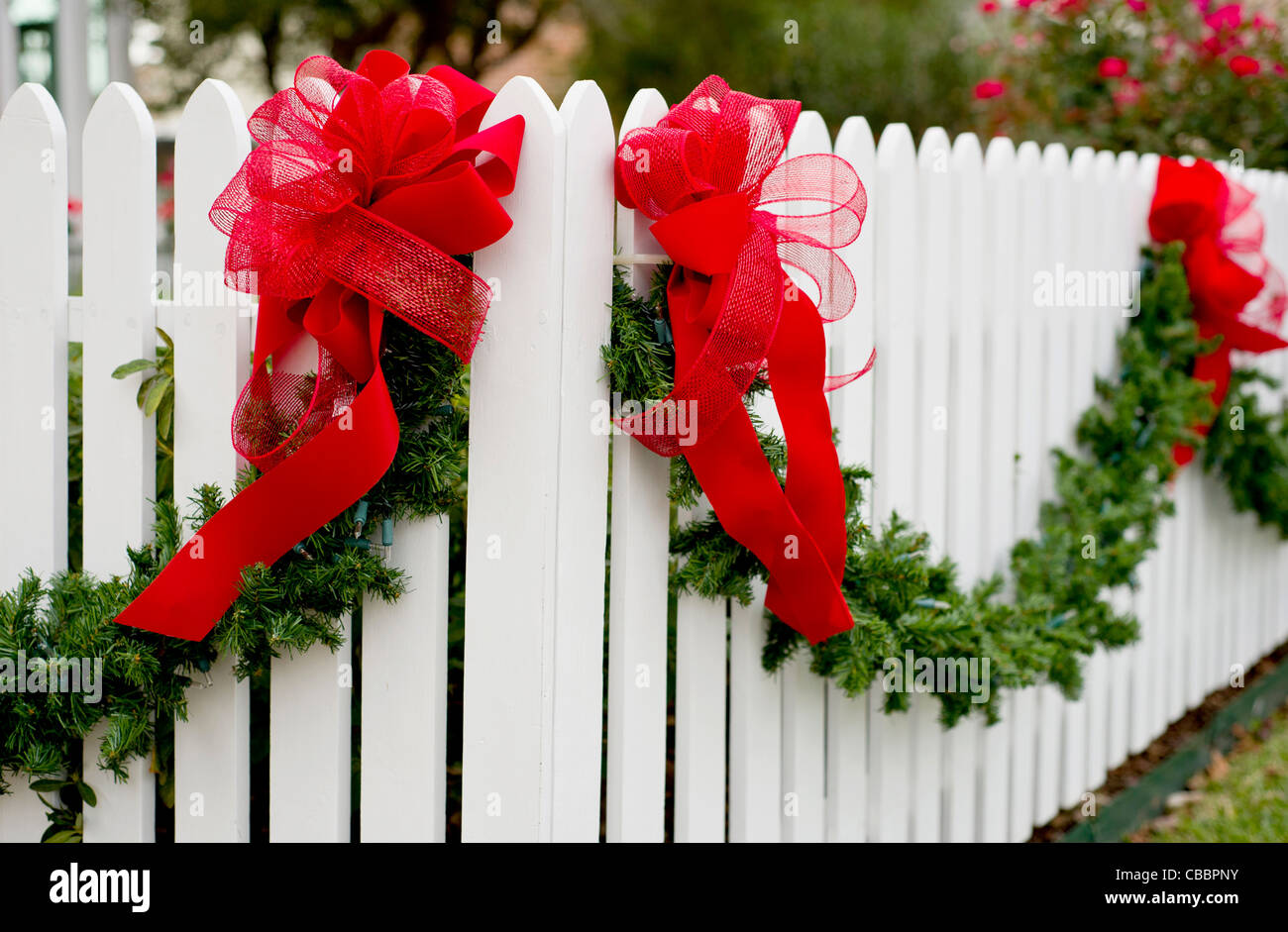 Garland et arcs rouge suspendu à une clôture blanche pour la saison des vacances. Banque D'Images