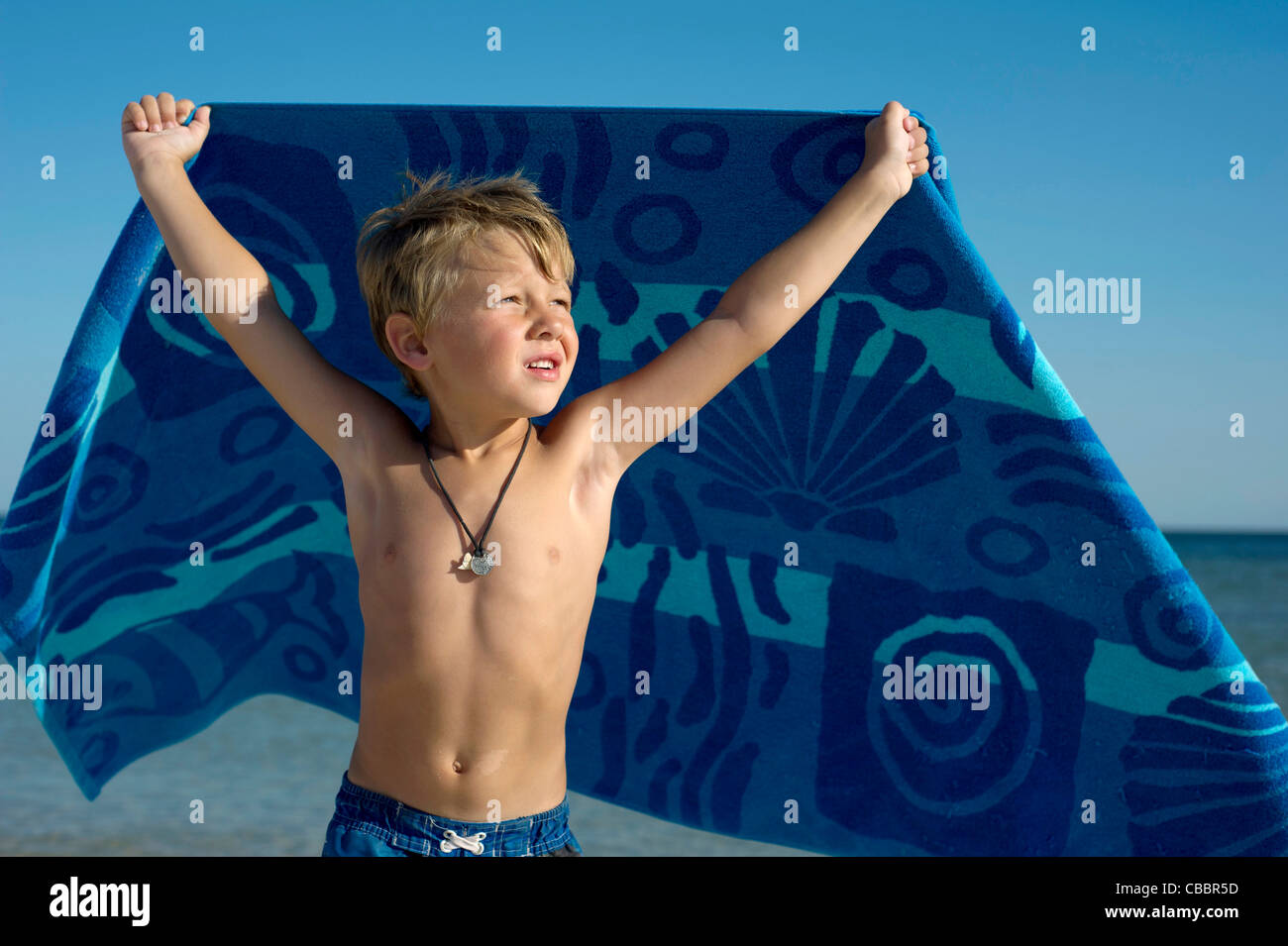 Un garçon est titulaire d'une serviette en se tenant debout en face de l'océan. Banque D'Images