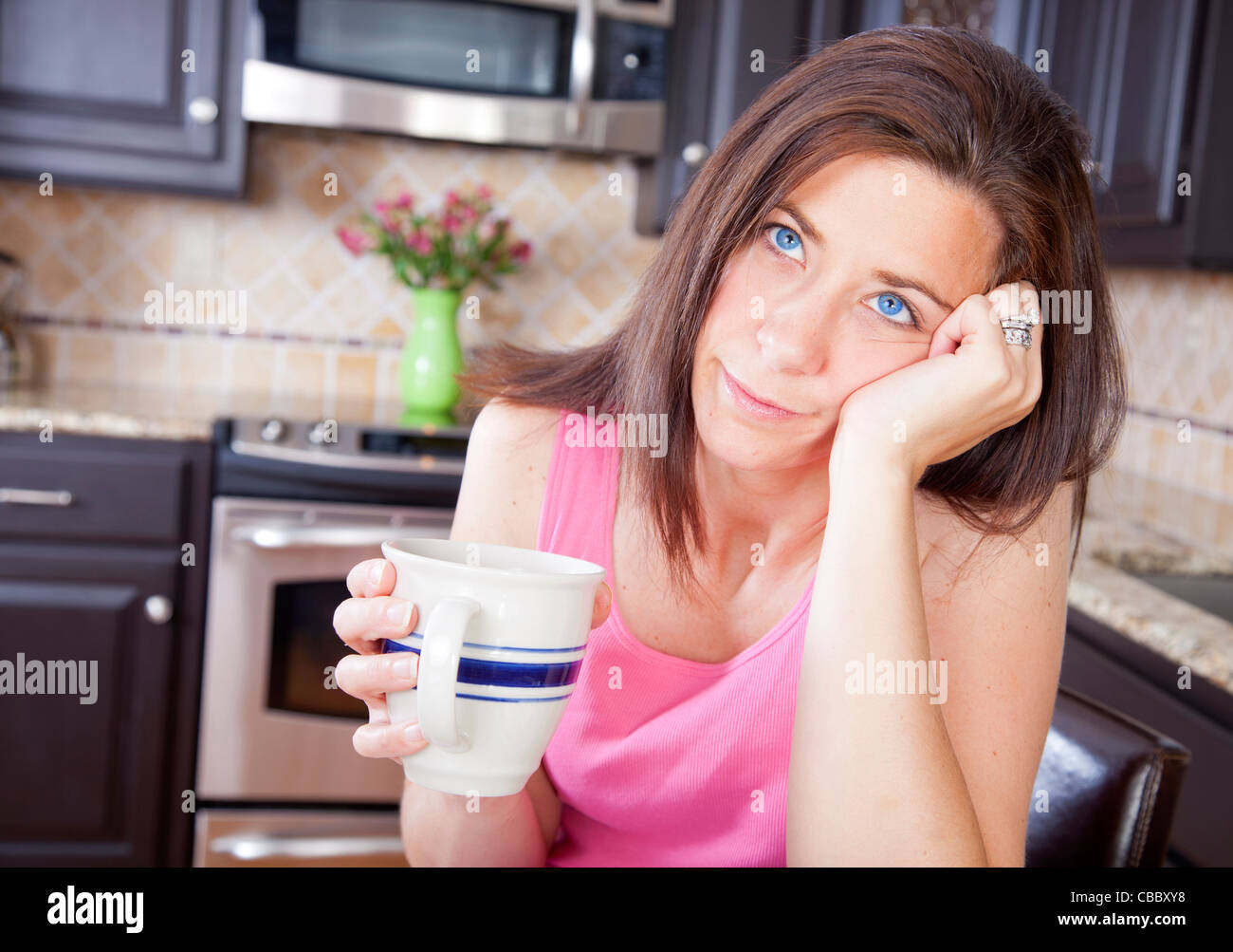 Bored femme assis dans la cuisine boire une tasse de café Banque D'Images