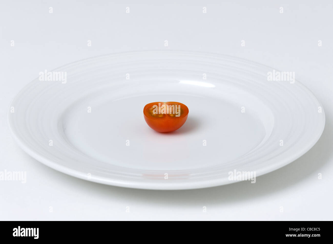 Un seul la moitié de tomate sur une plaque blanche sur un fond blanc. Banque D'Images
