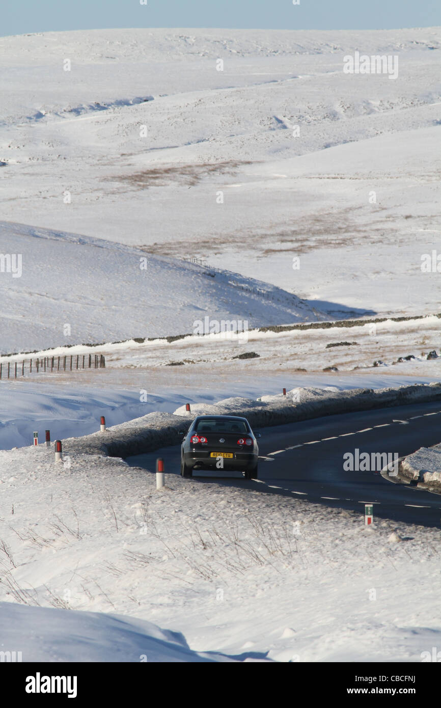 Une seule voiture qui roule le long de l'A628 Woodhead passer à travers des collines couvertes de neige Banque D'Images