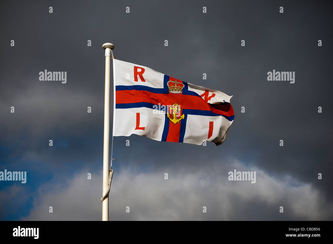 Drapeau de la RNLI contre un ciel noir, mât, poteau, bleu, ciel, couronne, emblème, d'ancrage Banque D'Images